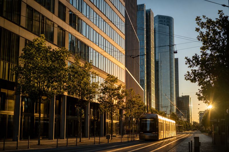 Bürotürme eines Geschäftsviertels im Abendlicht mit Tramlinie davor