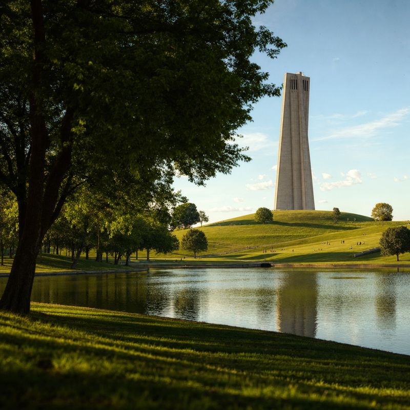 Großer Stadtpark mit einem schlanken Betonturm hinter grünen Hügeln